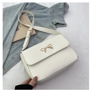 Détail du sac blanc à motif crocodile avec fermoir nœud doré sur fond en jean