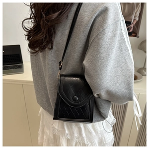 Quilted black leather crossbody phone bag shown worn by a model in a minimal home office