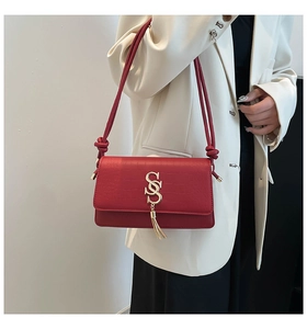 Detail of red croc-embossed shoulder bag featuring gold S-logo with a metal tassel charm
