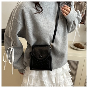 Detail of black quilted leather phone bag with round button flap and slim shoulder strap