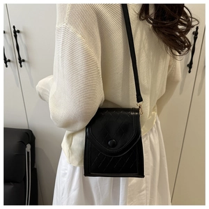Detail of a black quilted crossbody bag worn by a model against a white wardrobe background