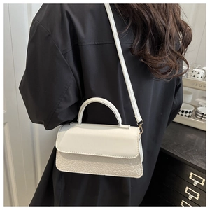 Detail of white faux leather handbag featuring crocodile pattern embossing on the flap