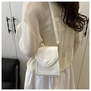 Detailed view of white embossed crossbody bag with U-shaped flap and circular buckle