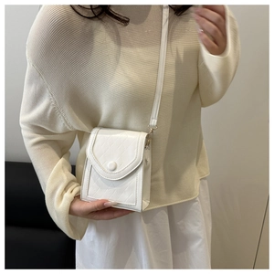 Close-up of a white quilted crossbody phone bag with fine shoulder strap and round buckle