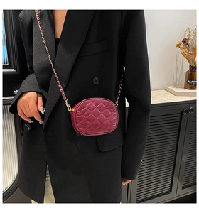 Close-up of a burgundy quilted camera bag with chain strap worn over a black blazer