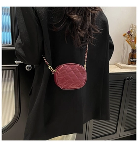 Detail of burgundy quilted round camera bag with gold chain strap on model shoulder