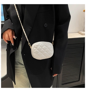 Detail of white quilted leather camera bag with gold woven chain strap on a black blazer