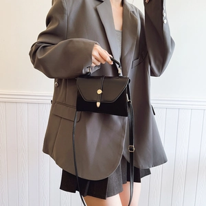 Mini sac bandoulière en cuir noir avec boucle dorée porté par un mannequin en tailleur