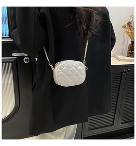 Detail view of a white quilted round chain bag worn with a black blazer for style