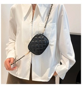 Close-up of a mini quilted black crossbody bag with a metal chain strap on a white shirt