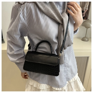 Detail of a black crossbody bag showing smooth leather flap and woven texture contrast