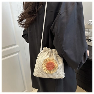 Detail of a woven straw bucket bag featuring a bright sunflower and drawstring strap