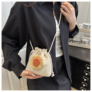Detail of woven straw bucket bag with sunflower accent and white crossbody drawstring strap