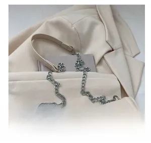 Detail der cremefarbenen Kunstledertasche mit Wellenklappe und gemischter Metallkette