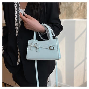 Detail of light blue crossbody bag with a decorative bow and elegant metal buckle