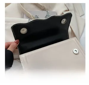 Detail der Wellenkantenklappe mit stabilen silbernen Magnet-Druckknöpfen an cremeweißer Tasche