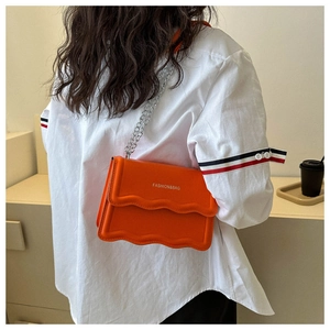 Detail der orangen Handtasche mit Wellenklappe und Silberkette, an einem Modell