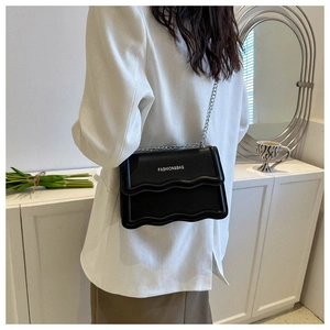 Detail der schwarzen Umhängetasche mit Wellenkanten-Design und silbernem Metallkettenriemen