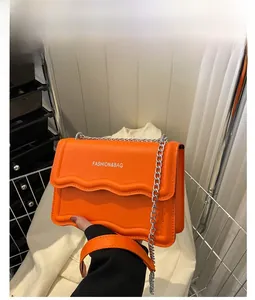 Detailansicht der orangefarbenen Umhängetasche mit Wellenklappe und Silberkette