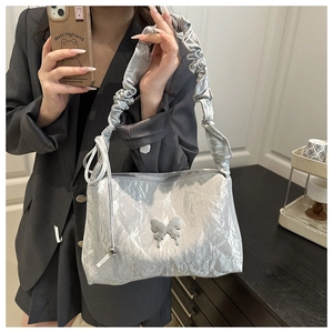 Détail d'un sac baguette argenté métallisé avec bandoulière plissée et papillon
