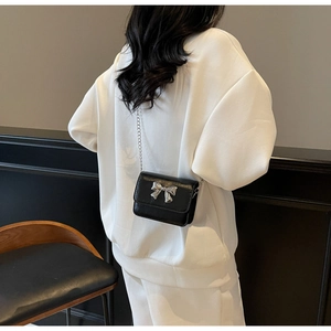 Détail du sac bandoulière noir avec nœud argenté porté par le mannequin de dos