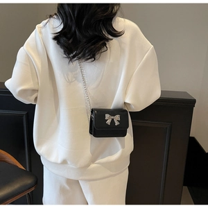 Detail of a mini black crossbody bag featuring a silver bow buckle and delicate metal chain