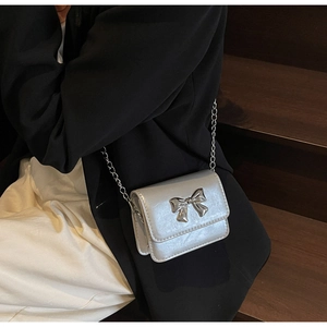 Silver mini crossbody bag with metallic bow detail and delicate chain strap on model