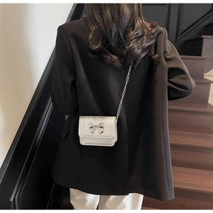 Vue arrière d'un mini sac argenté à chaîne avec nœud métallique sur un blazer noir
