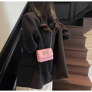 Close-up of a pink crossbody bag with a silver metal bow on a black blazer background