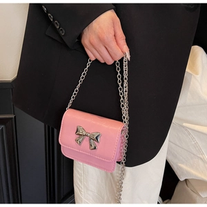 Macro view of a mini pink handbag featuring a silver metal bow and fine chain strap