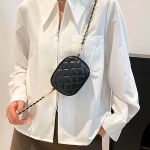 Chic black quilted camera bag with gold chain strap worn cross-body on white shirt