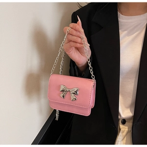Detail of a mini pink crossbody bag with a large silver metal bow and chain strap