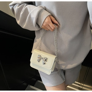 Detailed close-up of cream mini crossbody bag featuring a silver metal bow and chain strap