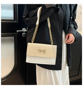 Detail of elegant shoulder bag with golden bow clasp and texture contrast flap