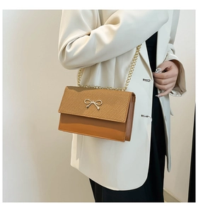 Detail of brown contrast shoulder bag with woven flap and gold bow chain strap