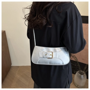 Silver metallic shoulder bag with gold buckle detail shown on a person in a modern home setting