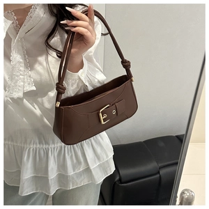 Detail einer dunkelbraunen Ledertasche mit goldener Schnalle und geknotetem Riemen