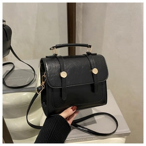 Détail d'un sac carré vintage noir avec texture brillante et deux boucles dorées