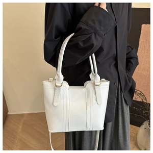 Close-up of minimalist white leather bucket bag with decorative stitching and gold hardware