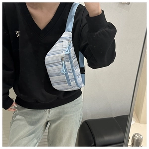 Detail of blue striped waist bag with double zippers and adjustable strap on a person