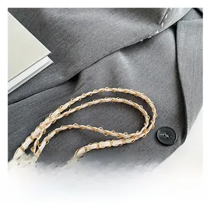 Close-up of woven gold metal and beige leather chain strap on grey blazer fabric