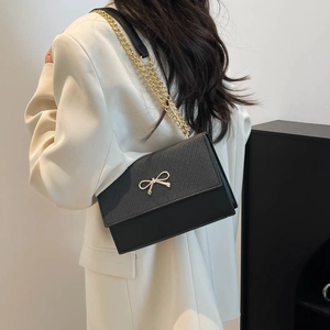 Minimalist black square crossbody bag with gold bow buckle and chain strap on model