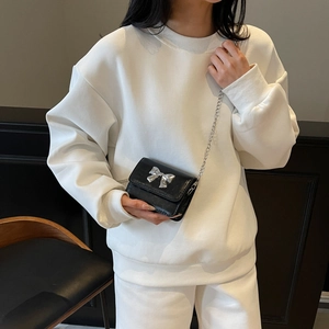 Mini black crossbody bag with silver bow accent and chain strap worn by a model