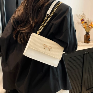 Minimalist beige and white crossbody bag with gold bow clasp and metal chain strap
