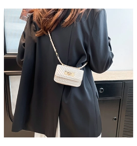 Detail of white quilted chain bag with gold hardware worn over a black blazer