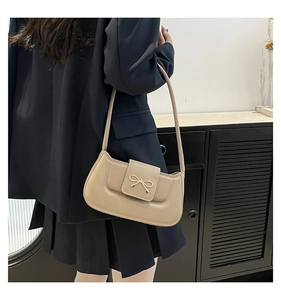 Close-up of beige bow-shaped metal clasp on a smooth synthetic leather shoulder bag