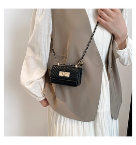Mini black quilted crossbody bag with gold chain strap shown on a white dress model