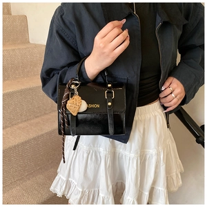 Detail of black patent leather handbag with gold buckle and fashion heart charm