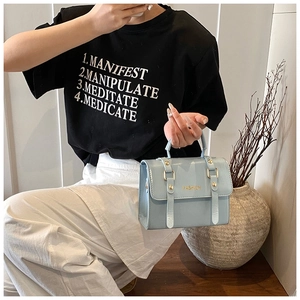 Detail of light blue rectangular crossbody bag featuring golden buckles and fashion text