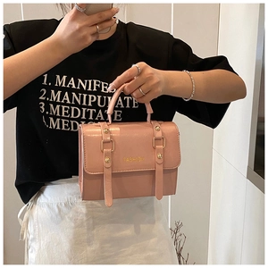 Detail of pink glossy leather handbag featuring golden fashion buckles and top handle